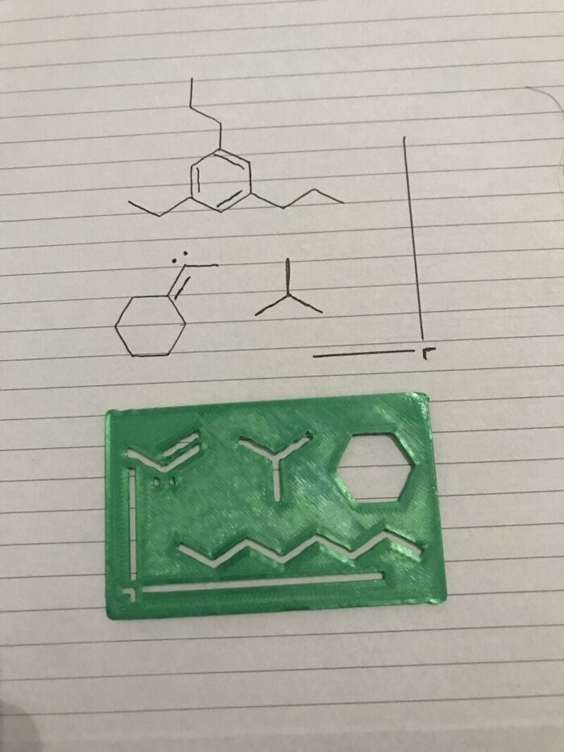 Green 3D-printed molecule model with hexagon and zigzag structures on lined paper.