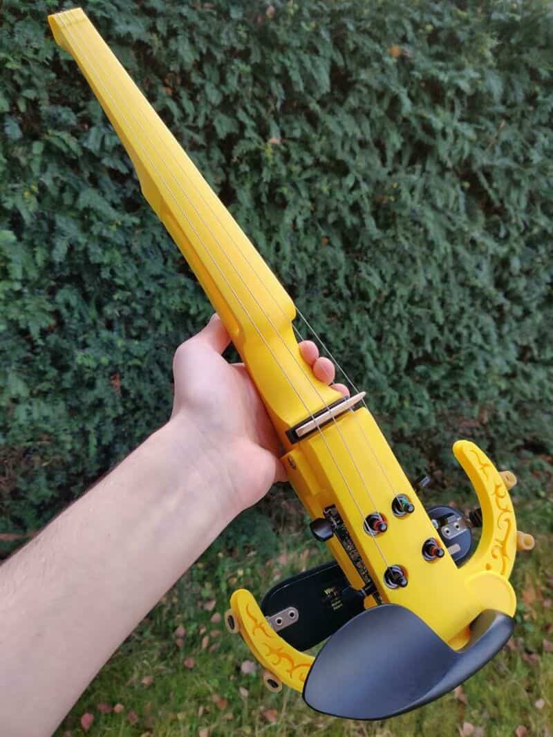 Yellow toy guitar with black strings and a black handle, held outdoors.