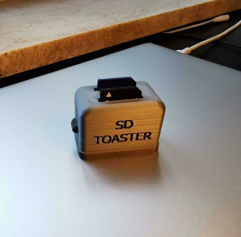 Small SD card toster with black switch, labeled 'SD TOASTER' on wooden surface.