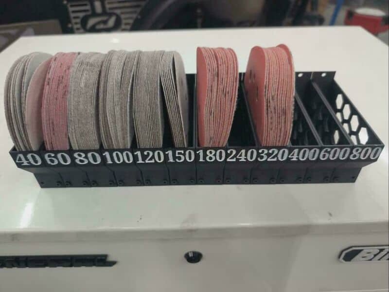 Assorted rolls of elastic bands in a black storage container on a white surface.