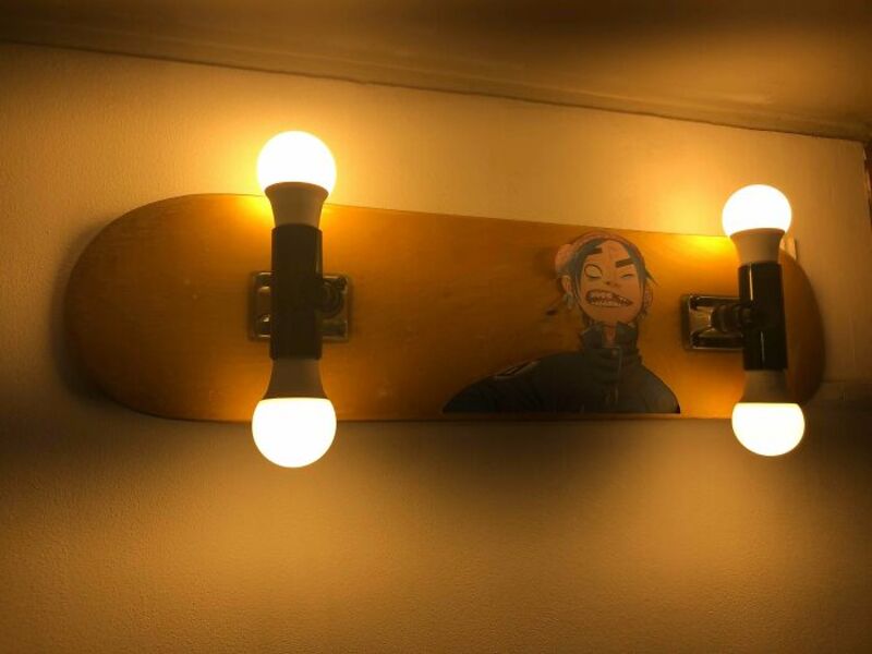 Wall-mounted light fixture with four bulbs and a skateboard with a cartoon face.