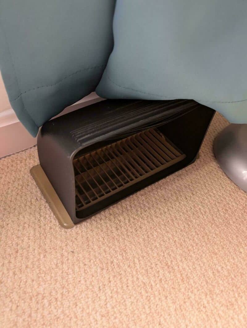 Black plastic space heater under a blue couch on beige carpet.