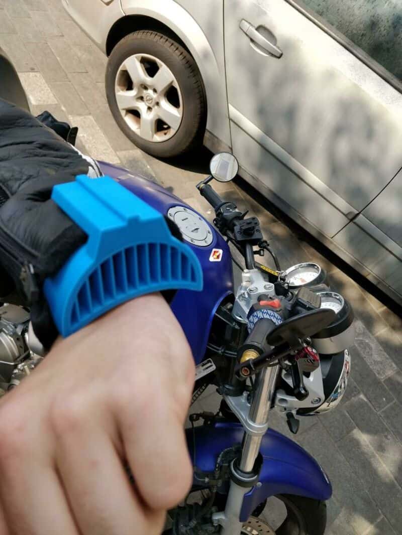 Close-up of a person on a blue motorcycle with a parking lot and silver car in background.