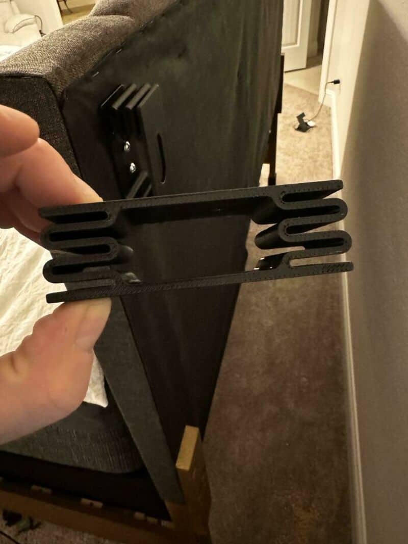 Person holding a black 3D printed object with multiple slots.