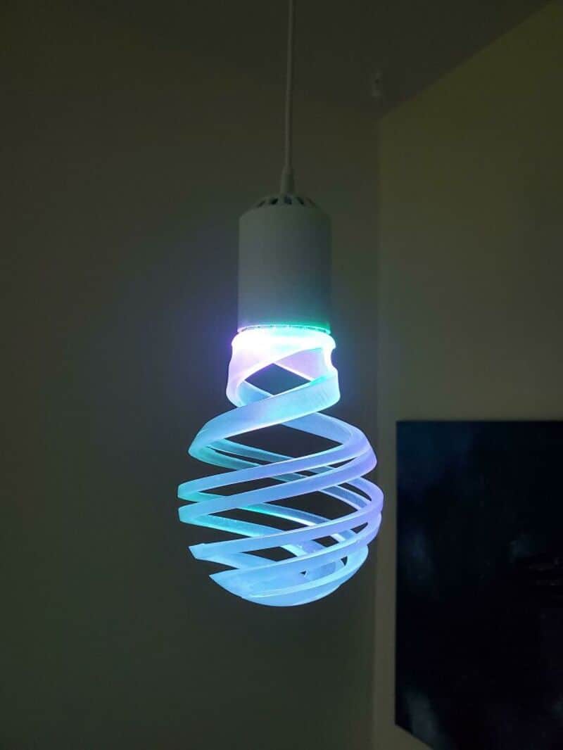 Colorful spiral LED pendant light hanging from ceiling in room.