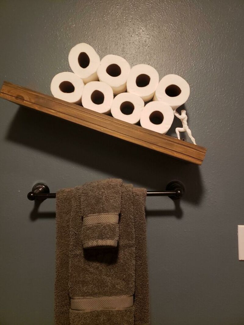 Stack of toilet paper rolls on a wooden shelf above a towel rack with a towel.