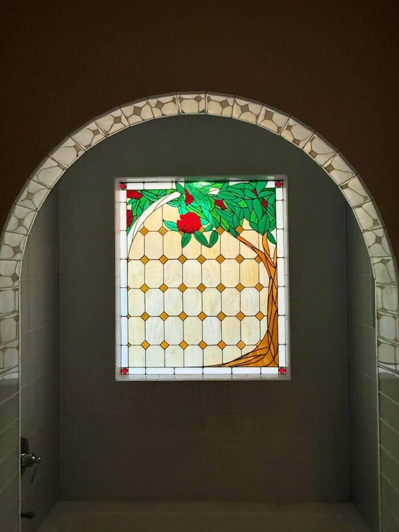 Stained glass window with a tree and red flowers in a bathroom.