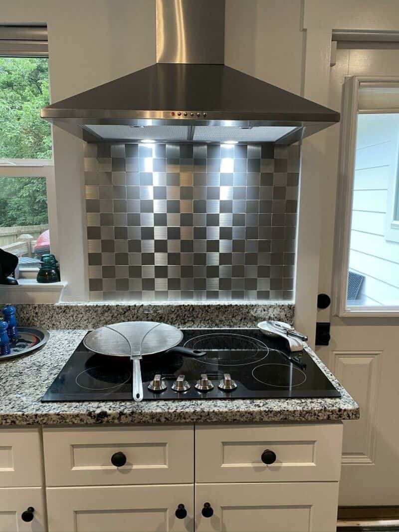 Modern kitchen stove with a stainless steel range hood and checkered backsplash.