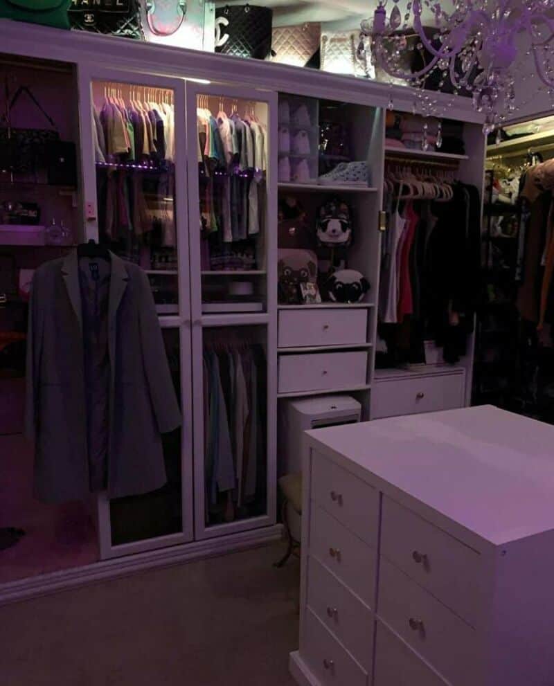 Closet with clothes, drawers, and a white table in a purple-lit room.