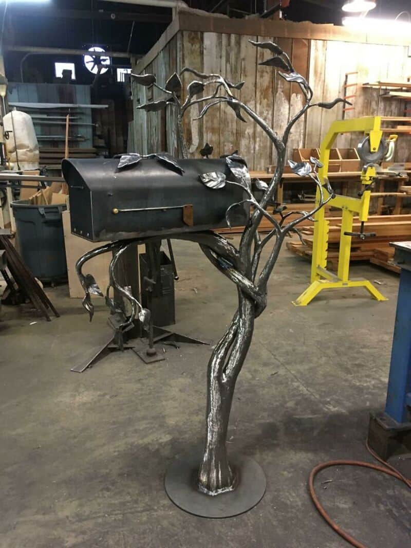 Metal tree-shaped mailbox with leaves, in a workshop setting.