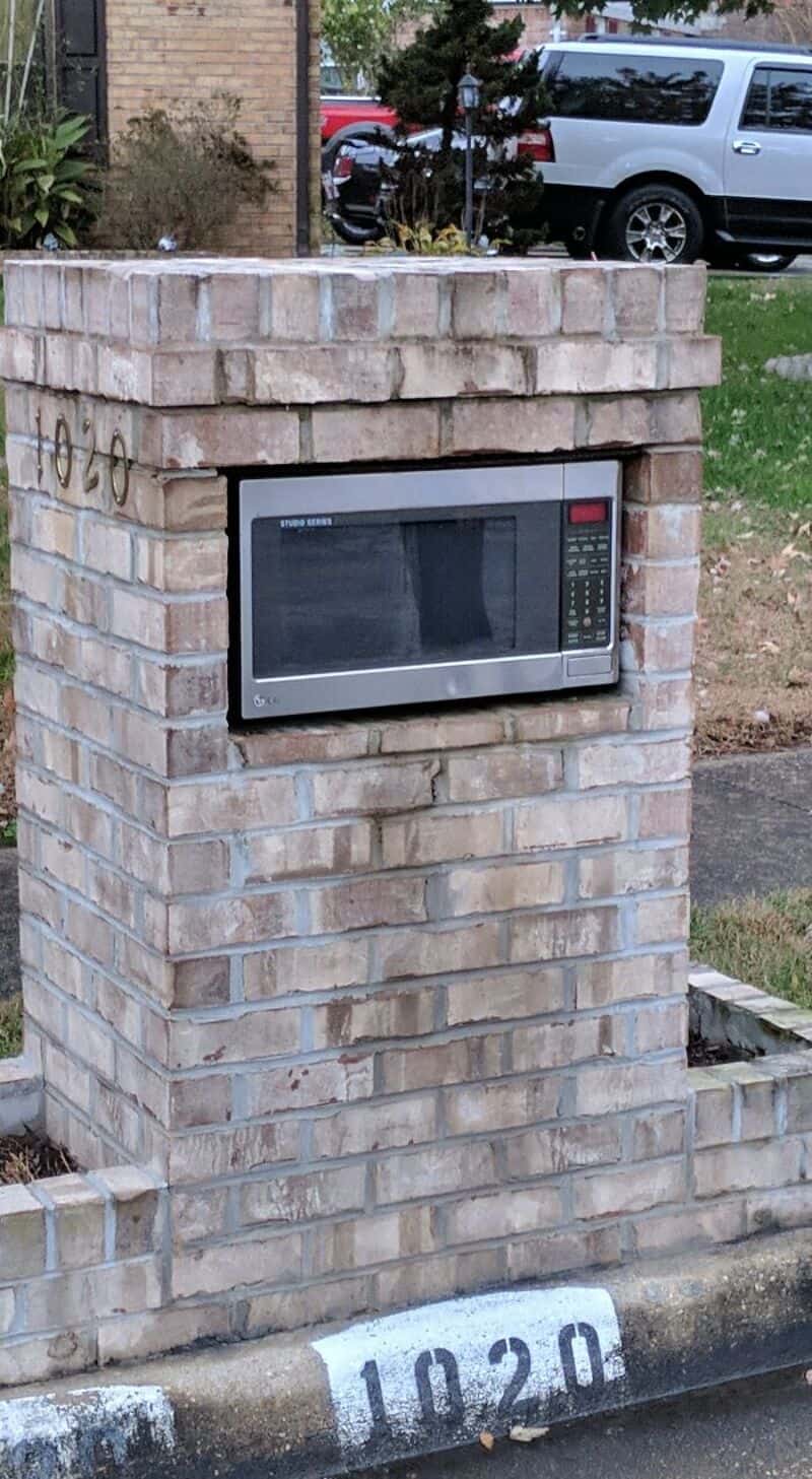 Microwave oven installed in a brick mailbox structure near the street.