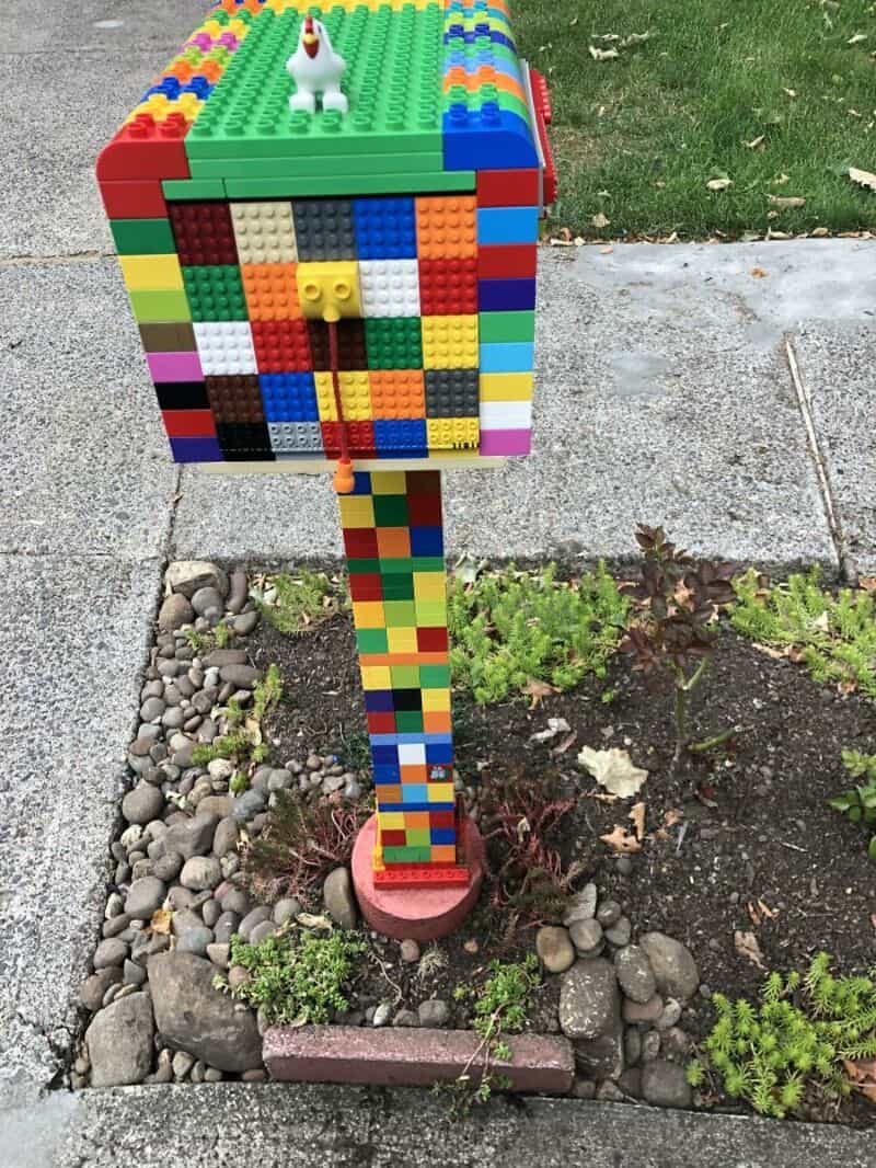 Colorful LEGO mailbox on a garden post with a white LEGO dog on top.