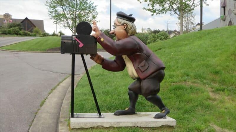 A statue of a man in a suit and hat mailing a letter at a mailbox.