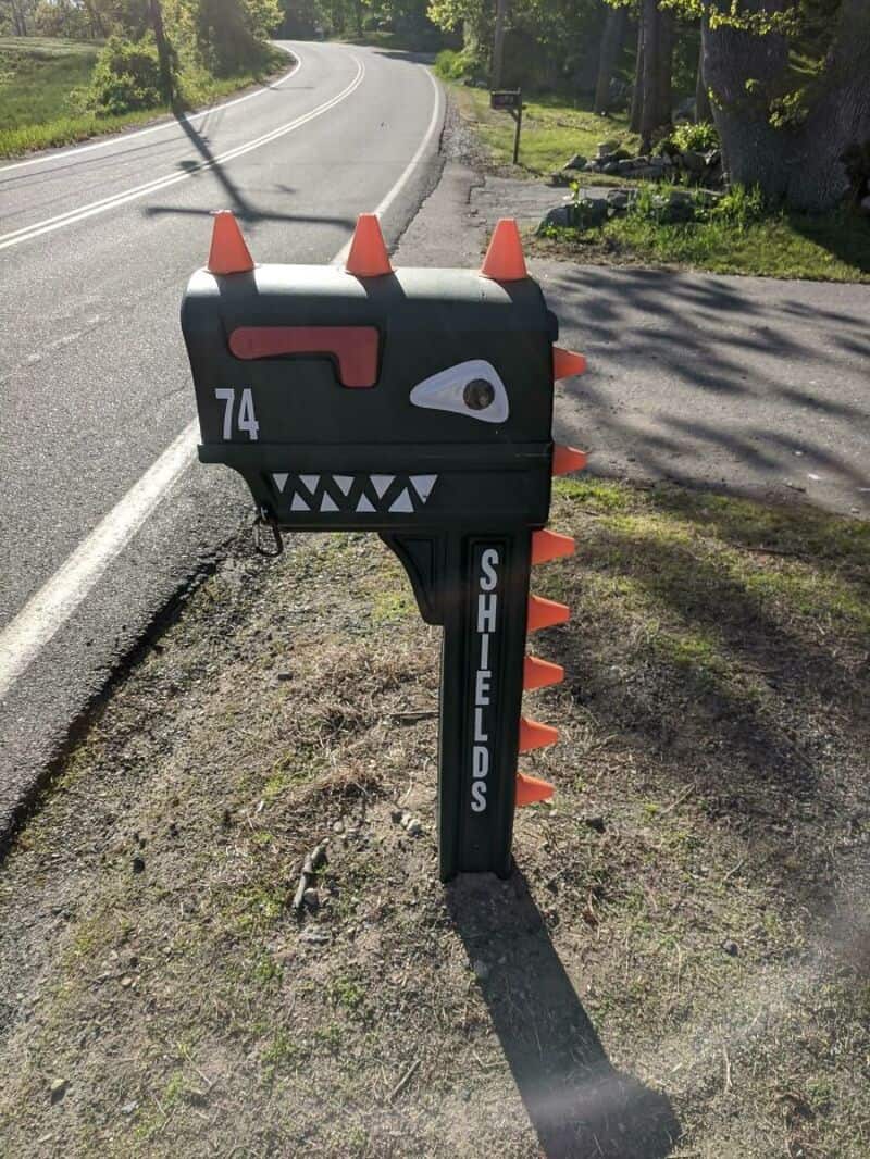 Mailbox designed as a monster with spikes, teeth, and a single eye, on a roadside.