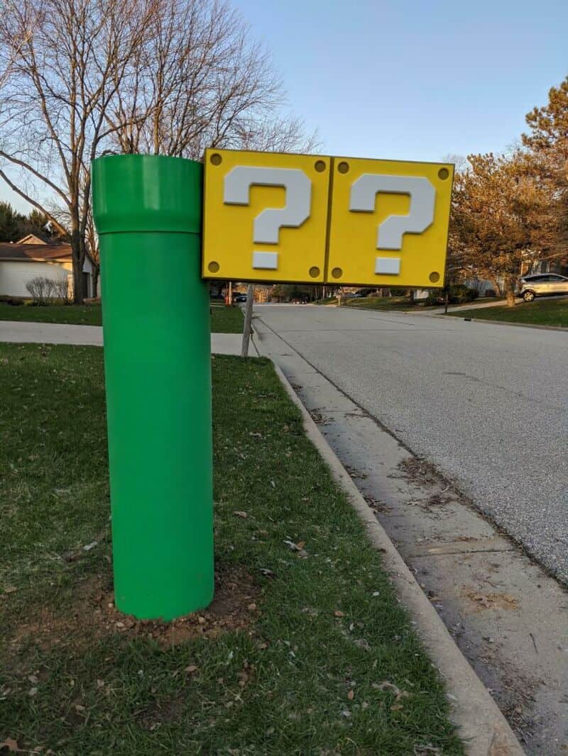 Green mailbox with two yellow blocks with white question marks on a sidewalk.