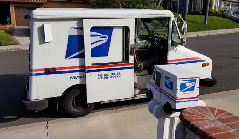 US Postal Service mail truck with open door and mailbox on sidewalk.