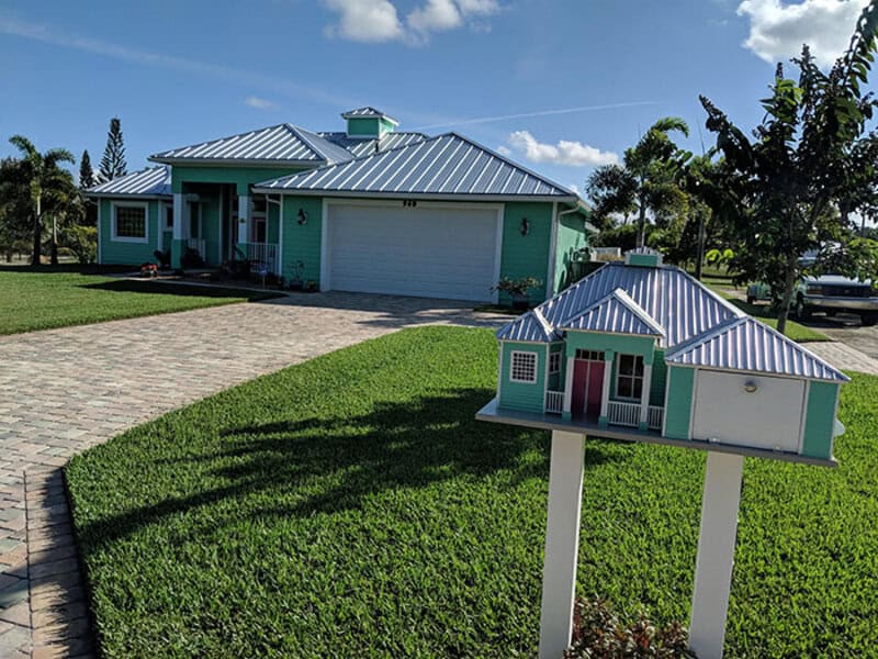 Colorful house with mailbox in front yard, blue sky, and trees.