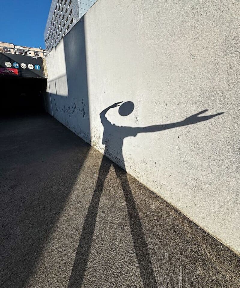 Shadow of a person playing with a ball on a white wall in an urban setting.
