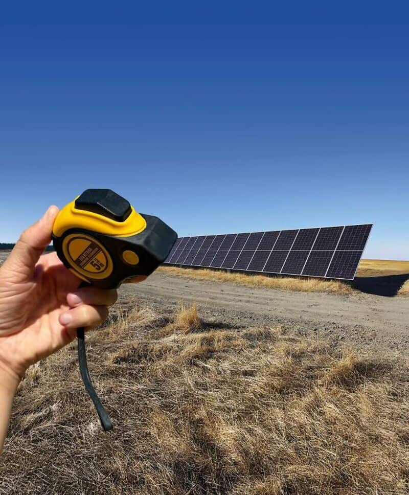 Person holding a yellow and black solar power meter in front of solar panels in a field.