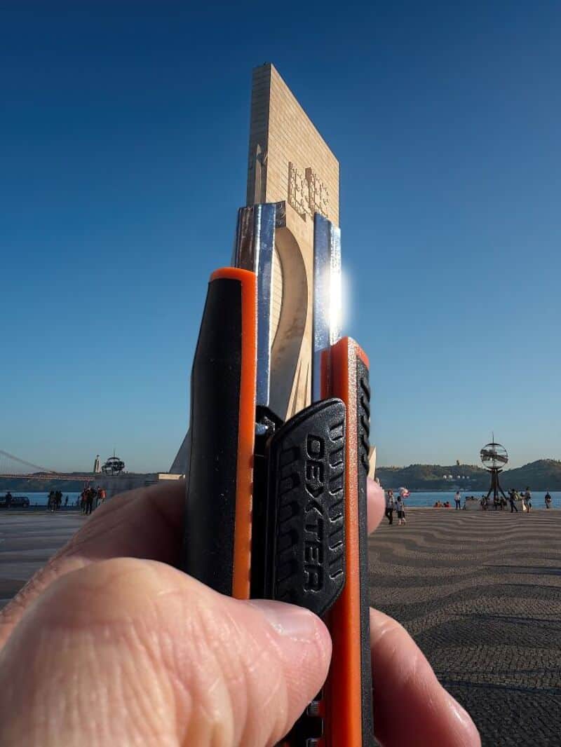 Hand holding a cutter knife in front of a monument at a waterfront.
