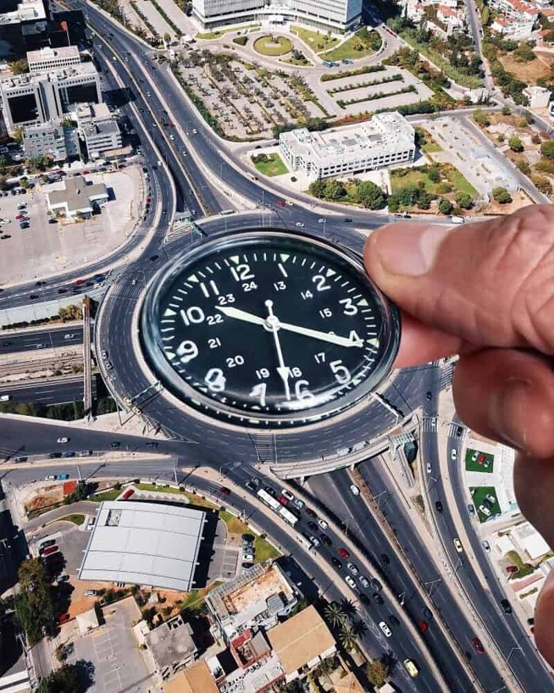 Person holding a clock over a cityscape with roads and buildings.