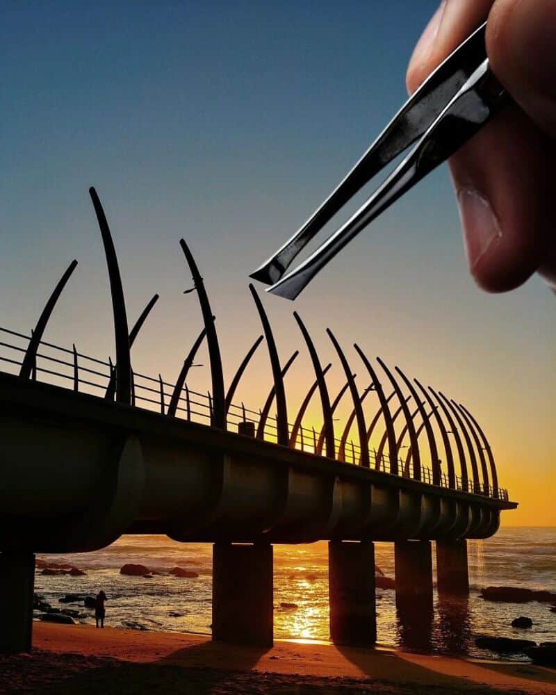 Giant hand with tweezers removing barbed wire from a pier at sunset.