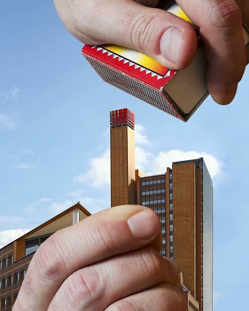 Close-up of a hand holding a matchstick above a tall building.