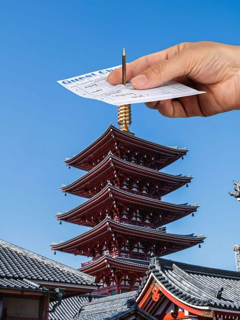 Hand holding a receipt above a traditional Japanese pagoda against a blue sky.