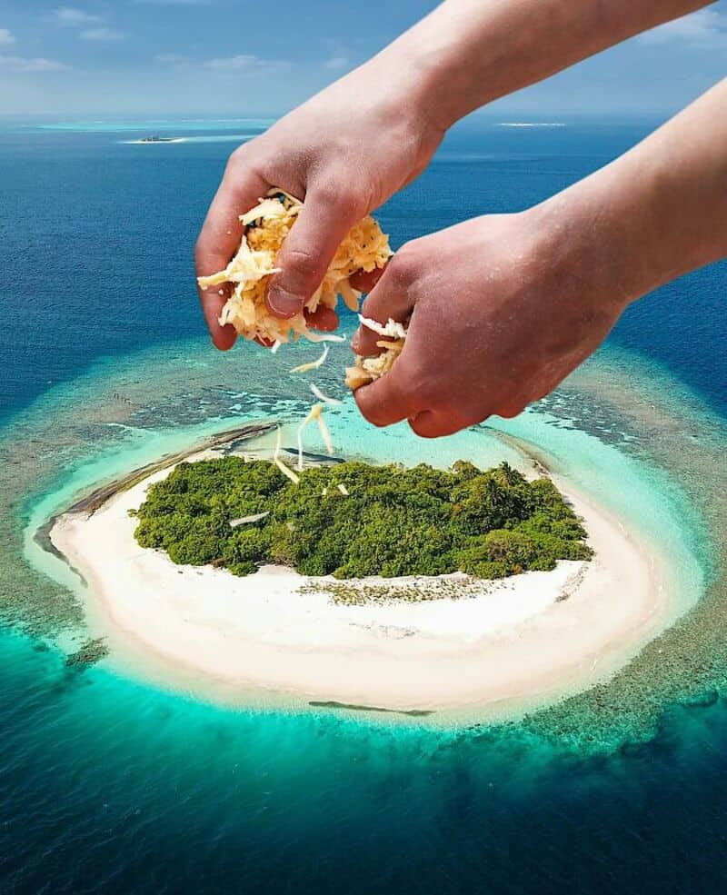 Hands holding bread over a small tropical island surrounded by turquoise water.