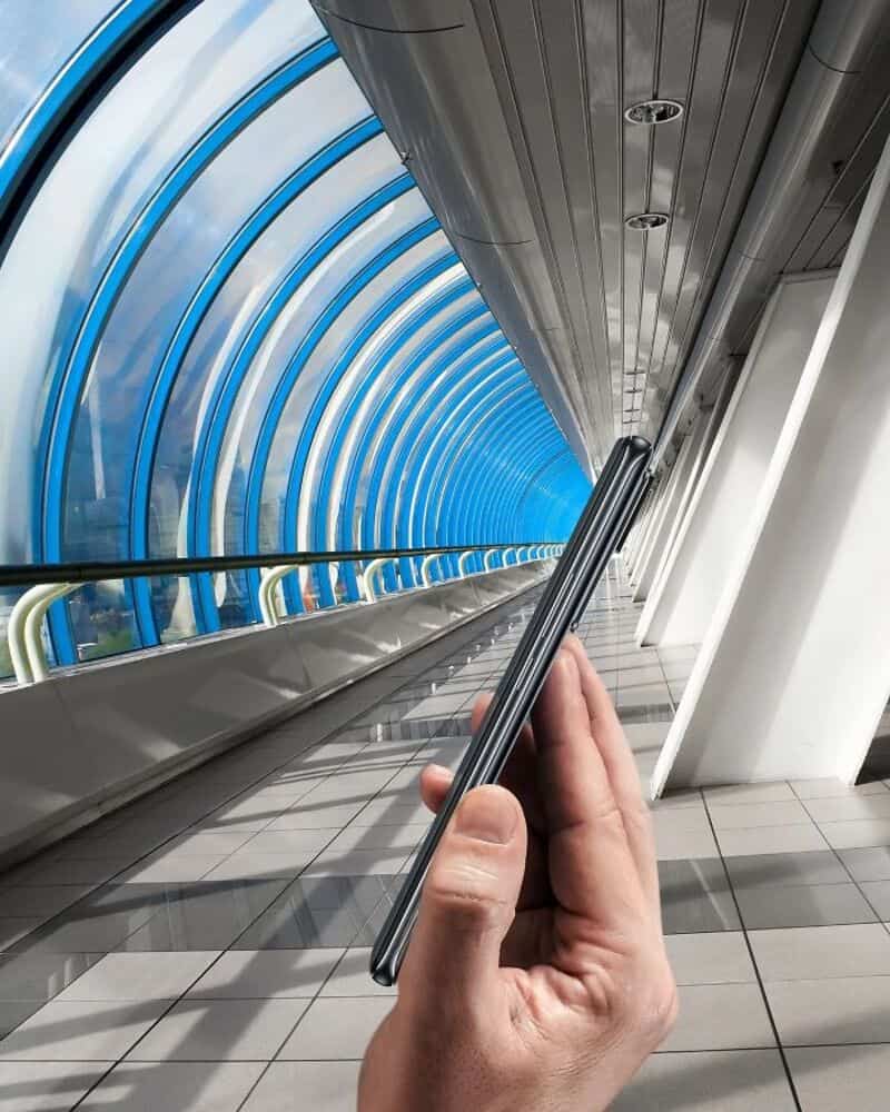 Person holding a smartphone in front of a futuristic tunnel with blue lights.