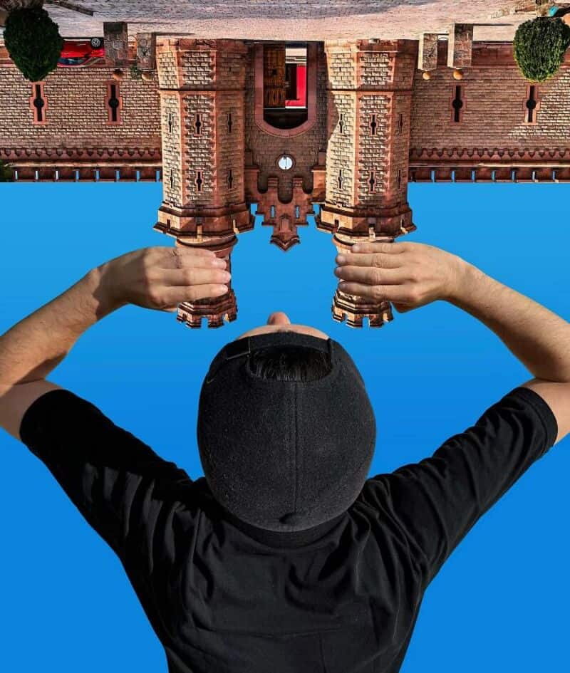 Person holding upside-down brick building model against blue sky.