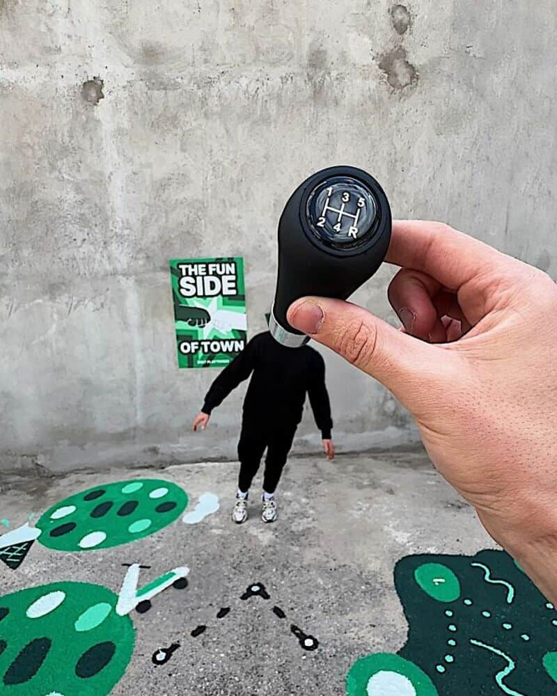Hand holding a gear shift knob over a street art scene with a person and painted mushrooms.