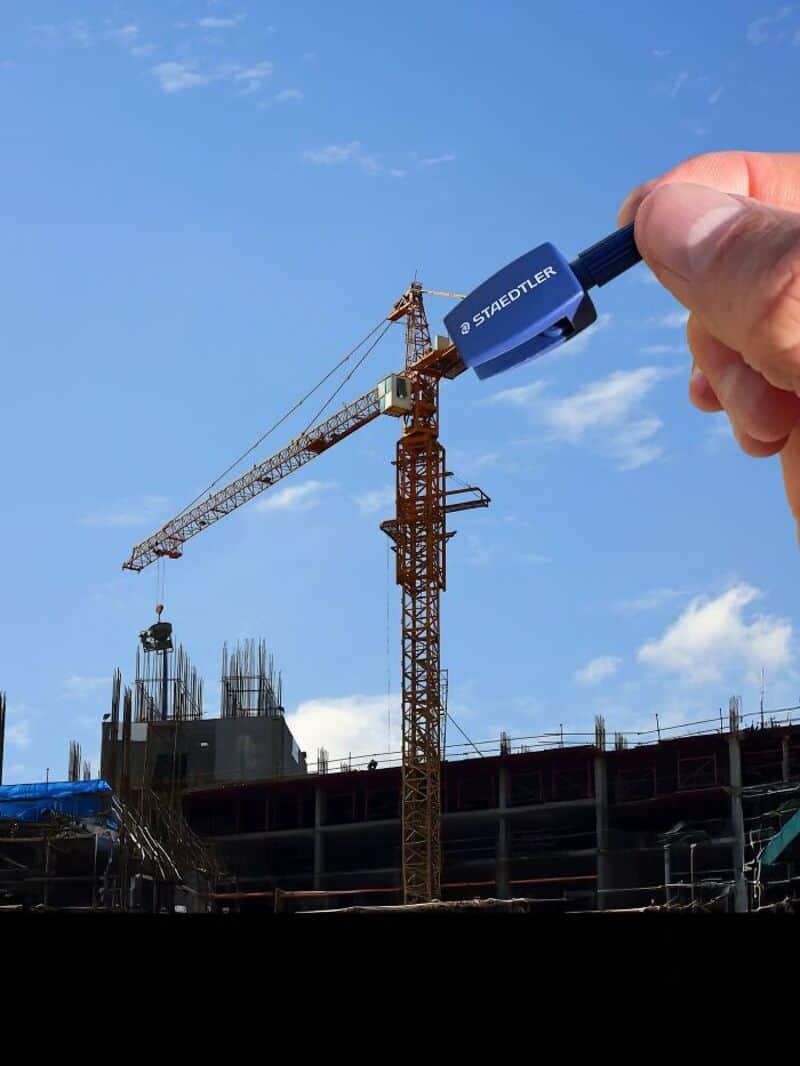 Construction site with crane and building under construction, hand holding a blue marker.