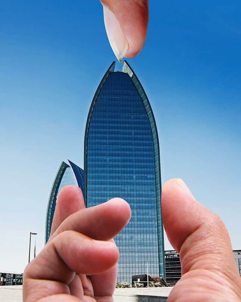 Giant hand pinching a miniature skyscraper against a blue sky.