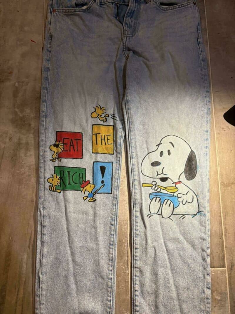 Light blue jeans with Snoopy and Peanuts characters painted on them.