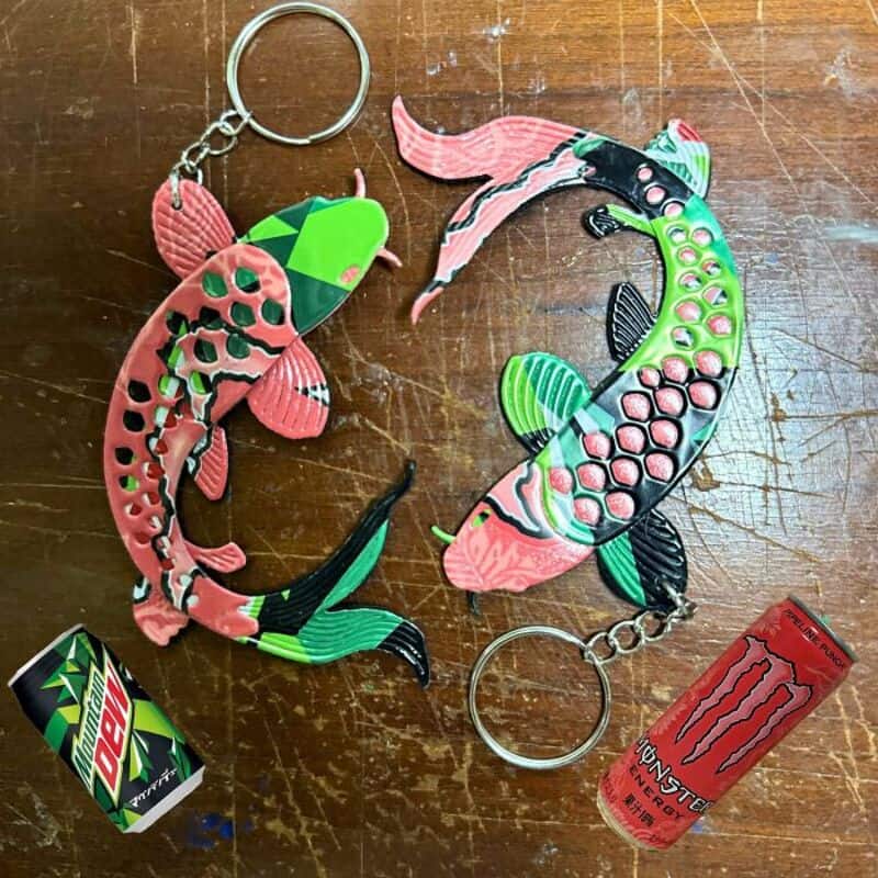 Colorful fish-shaped keychains with a Monster energy drink can and a small box on a wooden surface.