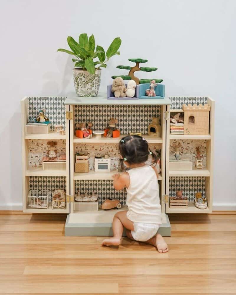 Child playing with wooden dollhouse and toys on a shelf.