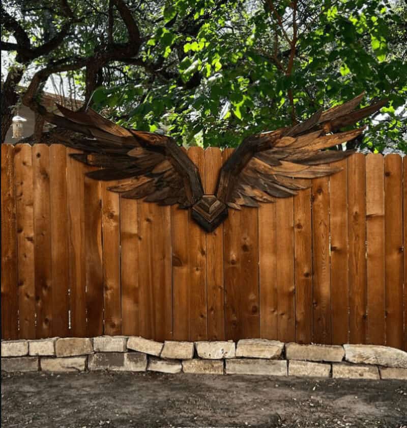 Wooden fence with a wing-shaped decoration made of dark wood pieces.