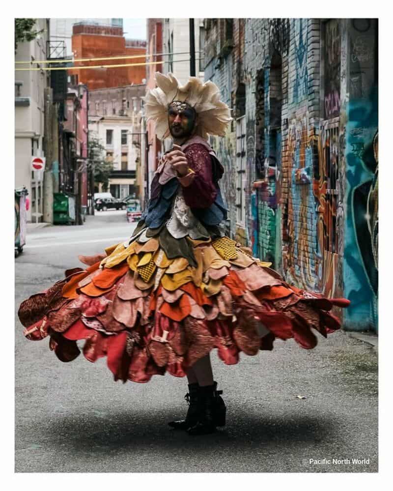 Person in colorful upcycled costume with layered fabric skirt on city street.