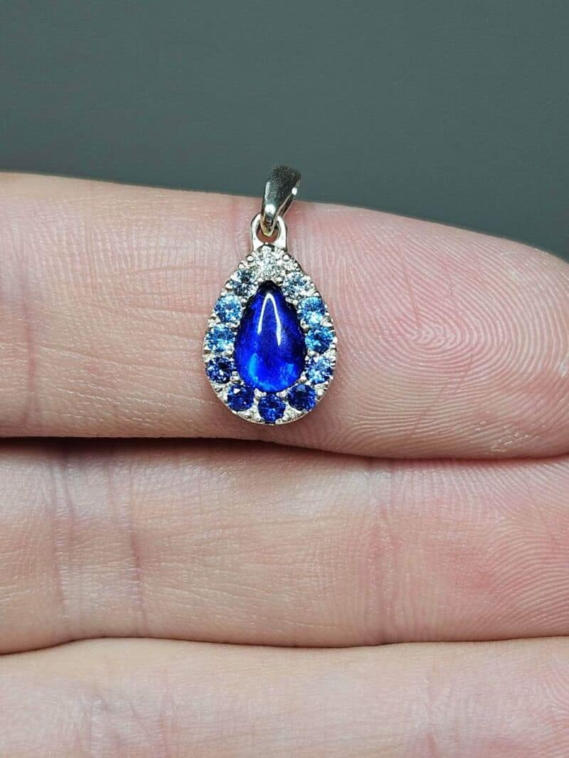 Silver pendant with blue teardrop-shaped gemstone and surrounding clear stones.