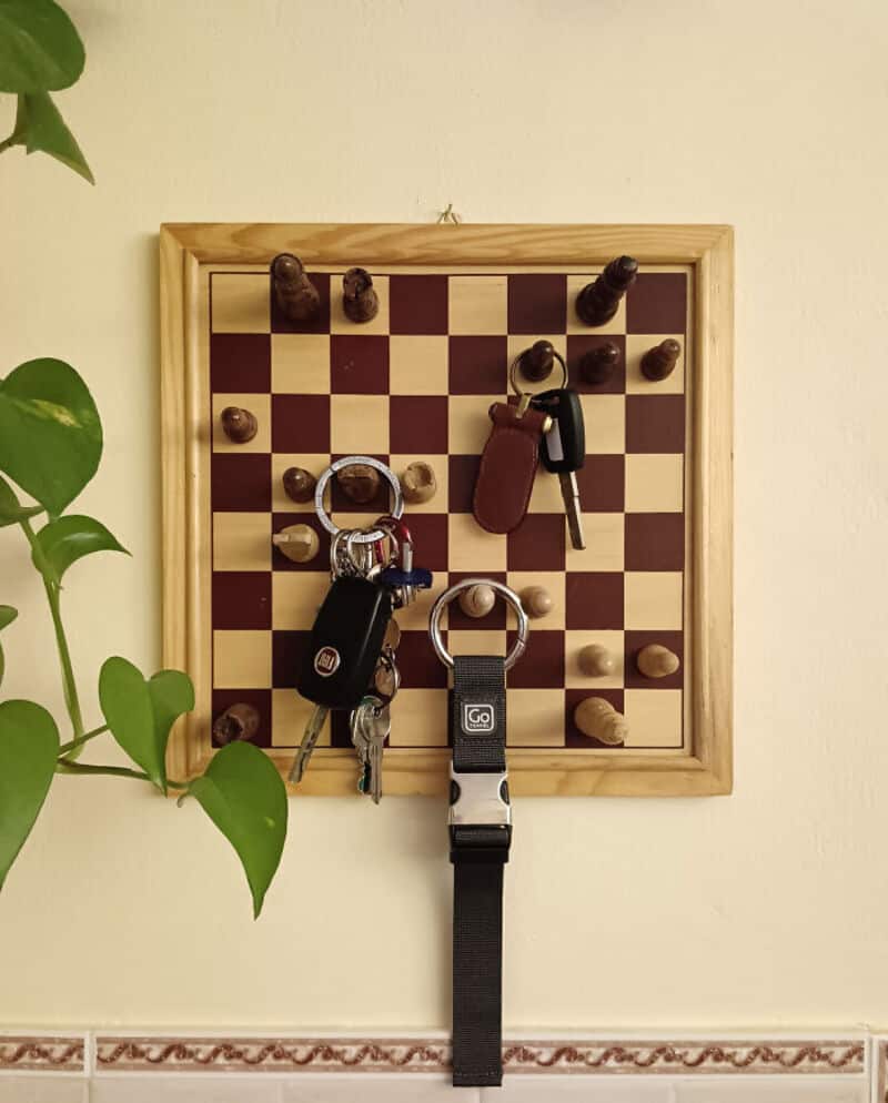 Chessboard with keys and keychains hanging on wall, with a plant on the side.
