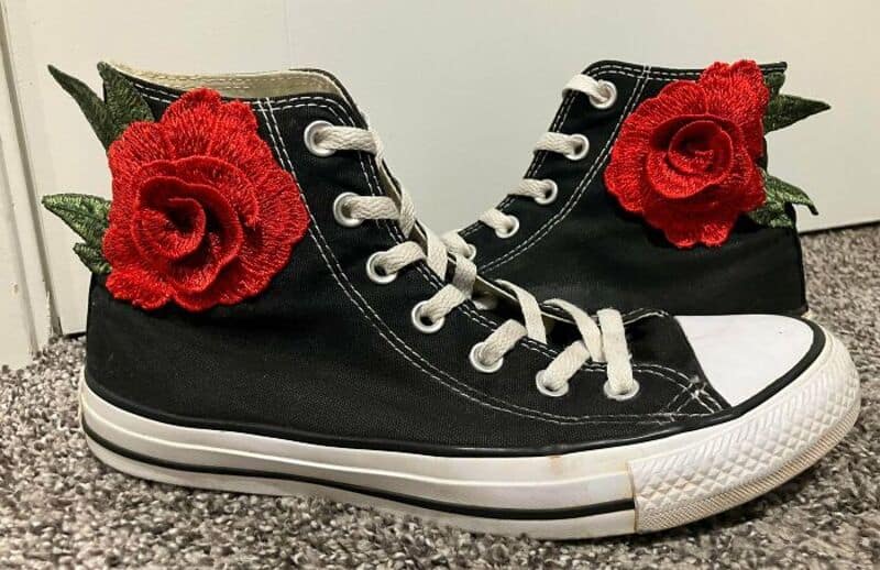 Black sneakers with red fabric roses and green leaves on the sides.