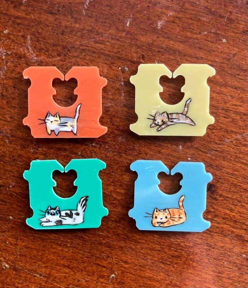 Four colorful cat-shaped clips with different cat illustrations on a wooden surface.