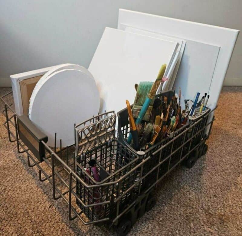 Art supplies in a black cart including brushes, canvases, and paper for upcycling crafts.