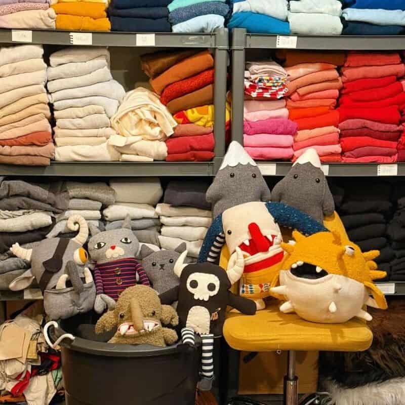 Colorful plush toys and stuffed animals on a yellow chair in front of shelves of folded clothes.
