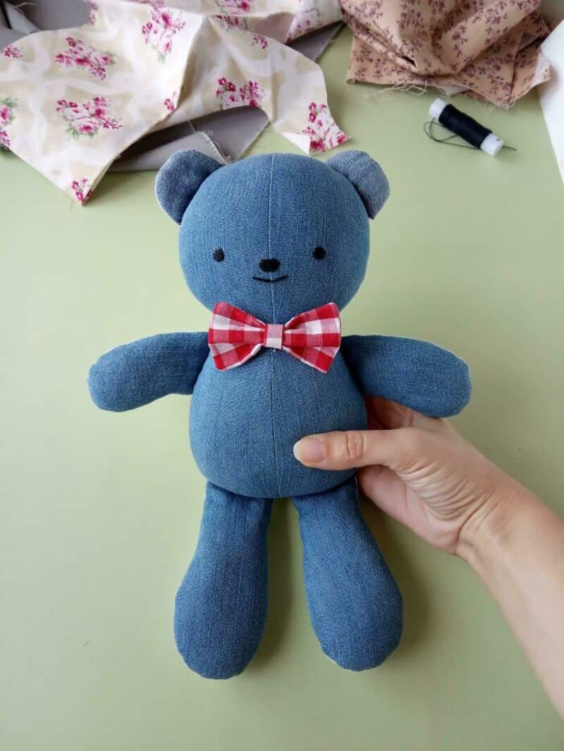 Blue teddy bear with a red and white checkered bow tie held in hand.