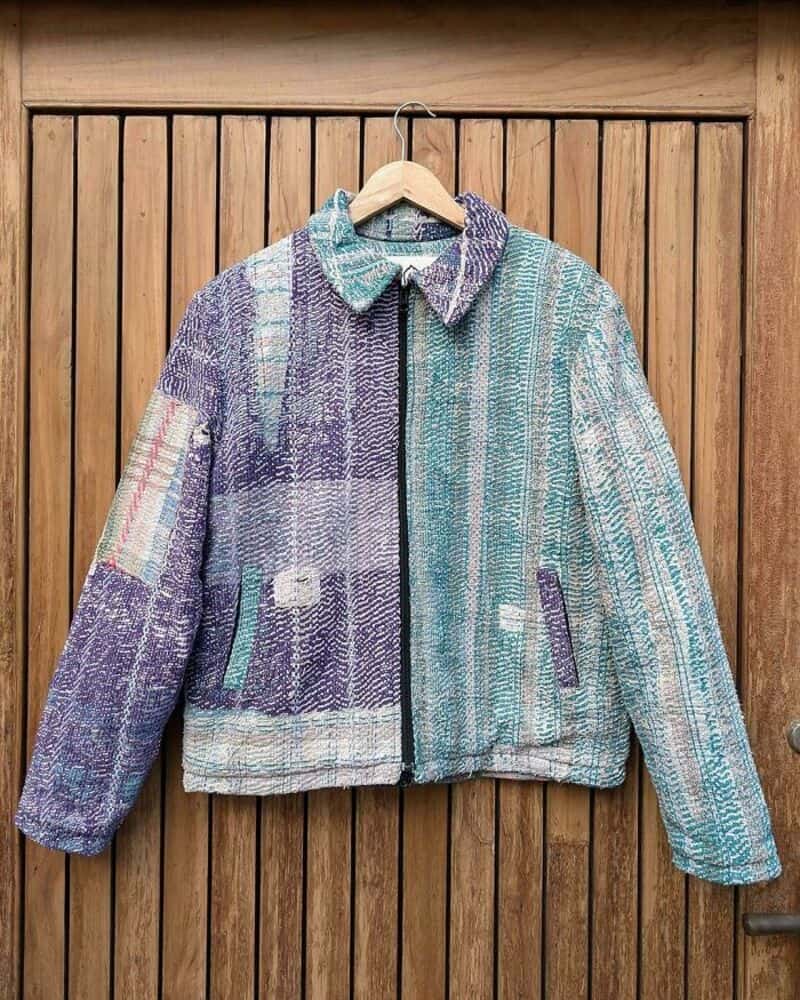 Colorful patchwork upcycled jacket hanging on a wooden wall.
