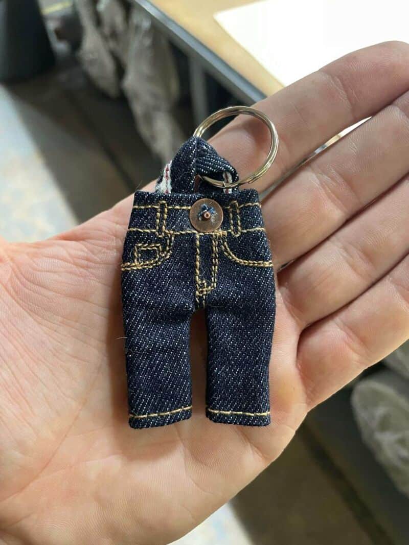 Miniature jeans keychain with gold stitching and a button, held in hand.