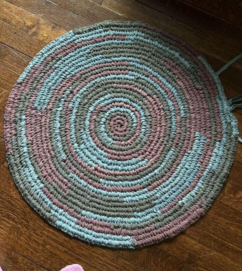 Colorful braided circular rug with pink, blue, and beige tones on wooden floor.