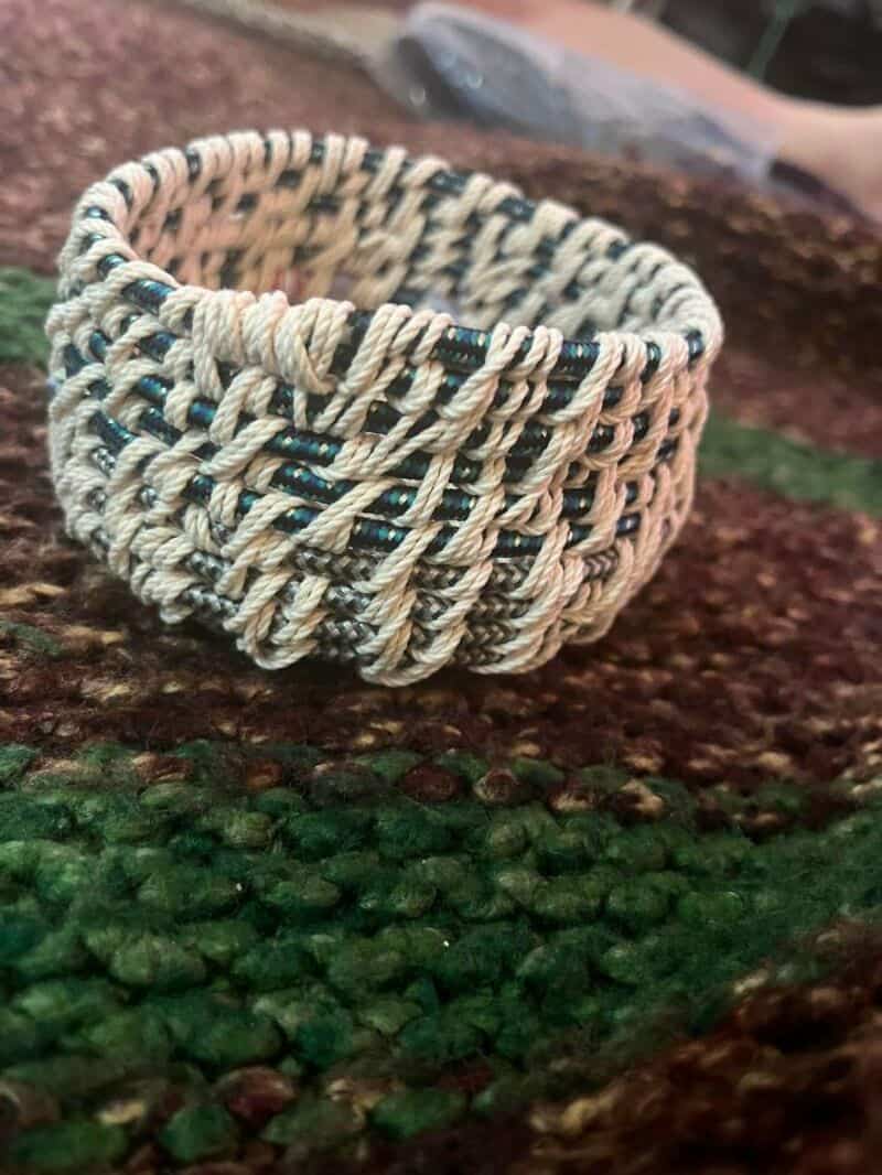 Handwoven bracelet made of beige and black threads on a textured surface.
